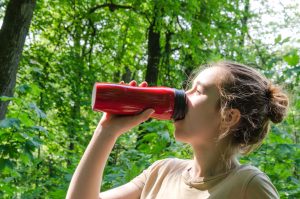A young girl drinks water from a reusable bottle. Horizontal bac